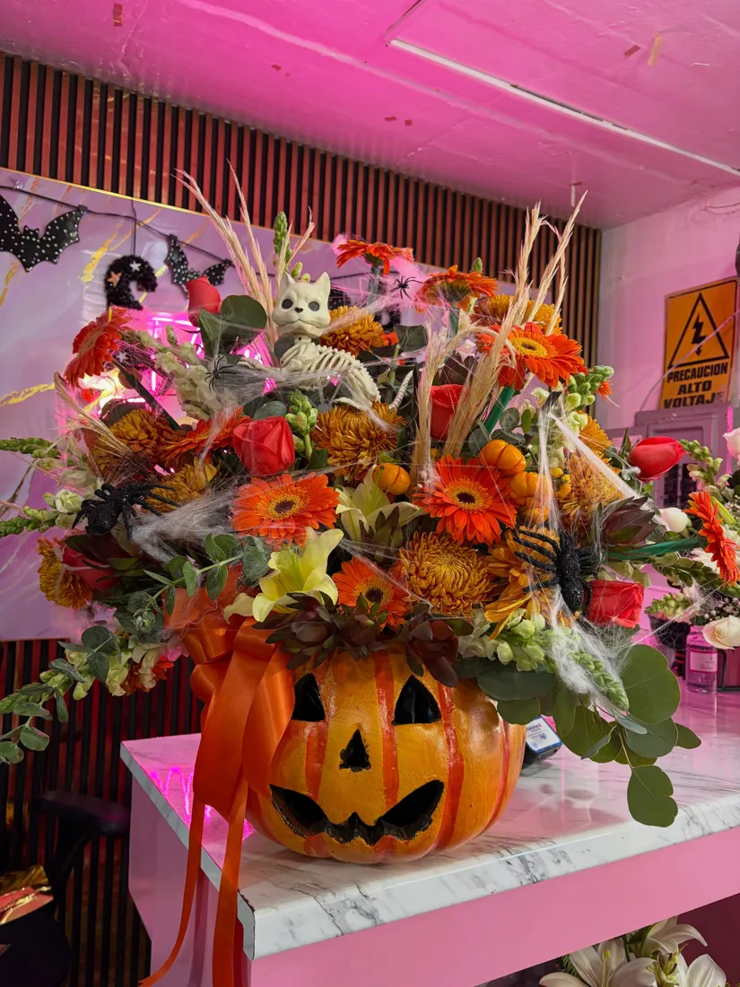 Arreglo floral de temporada en una calabaza: gerberas naranjas, crisantemos, rosas rojas, eucalipto y decoración de telarañas