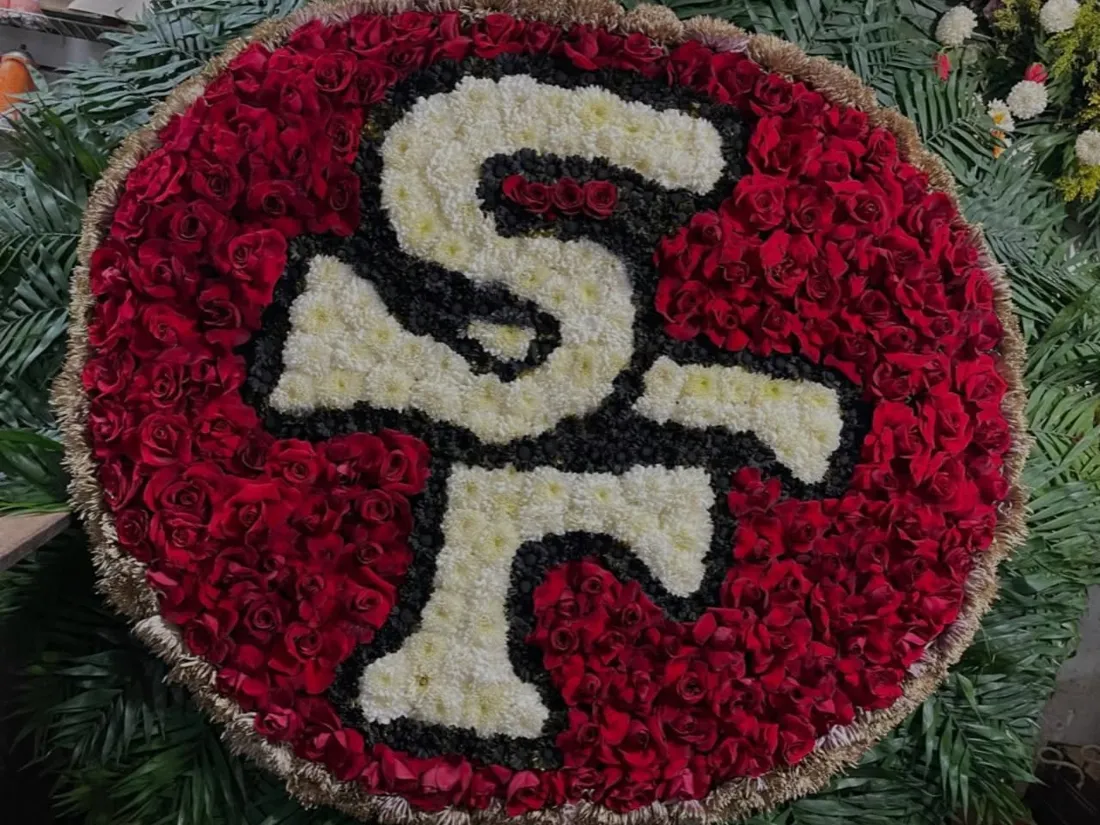 Corona floral circular personalizada con un logo deportivo hecho con rosas rojas, crisantemos blancos y negros y borde dorado
